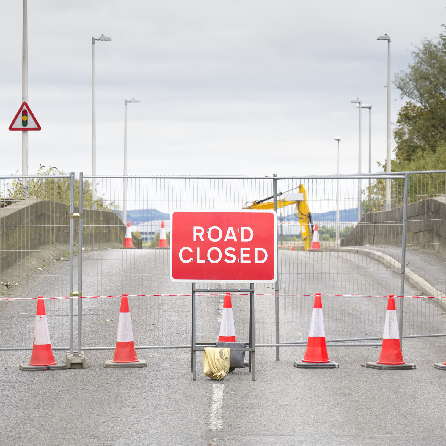 Road ahead closed sign with traffic cones and red barrier fence crossing UK